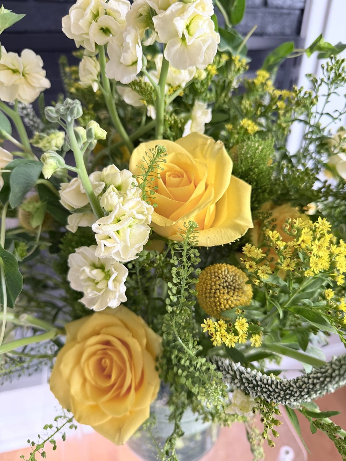 Close view of yellow roses, white stock, and green seasonal stems